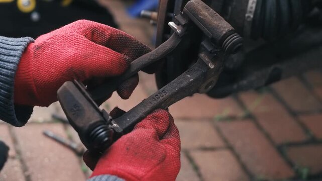 Inspecting rusted brake caliper bracket after removal during vehicle repair. Examining worn mounting hardware for corrosion damage and maintenance assessment outdoors. Automotive mechanical inspection