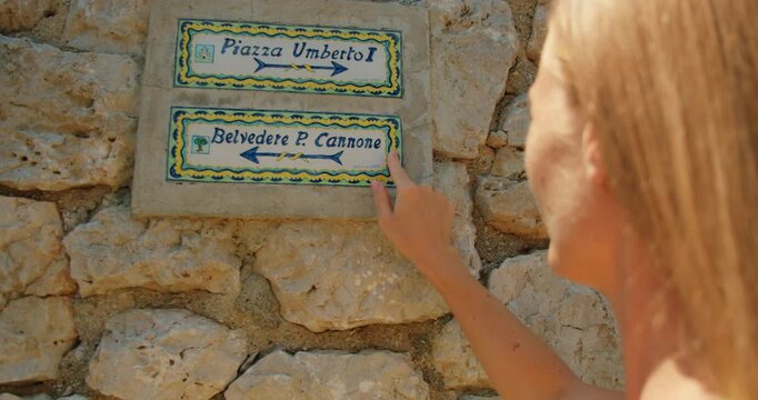 A traveler points to summer signs for Piazza Umberto I and Belvedere di Punta Cannone during tourist tour in Capri