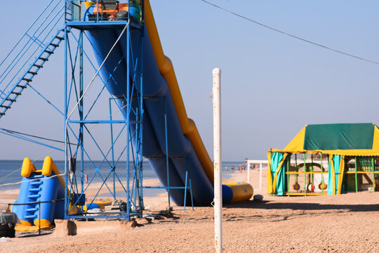 Water slide rises on sandy beach near sea, summer recreation scene. Slide attraction stands in coastal resort setting, leisure concept, outdoor activity, vacation lifestyle background.