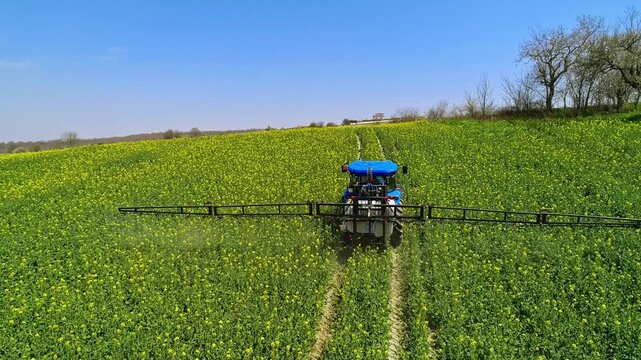 A drone view shows a tractor-mounted sprayer working on green farmland, performing agricultural spraying for crop protection, field maintenance, and modern farming practice.