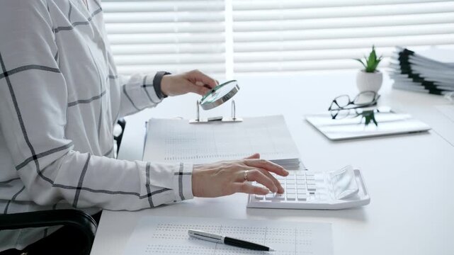 Financial professional carefully reviewing business documents with a magnifying glass while calculating numerical data, demonstrating diligent tax preparation and detailed audit analysis