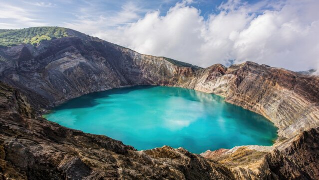 Turquoise crater lake in a volcanic caldera surrounded by rocky cliffs under a cloudy sky