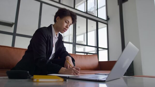 Businesswoman Taking Notes While Working on Laptop