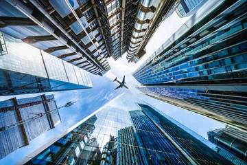 Low angle view of looking up directly at the skyline of the financial district in central London with an airplane in the sky passing by © moofushi