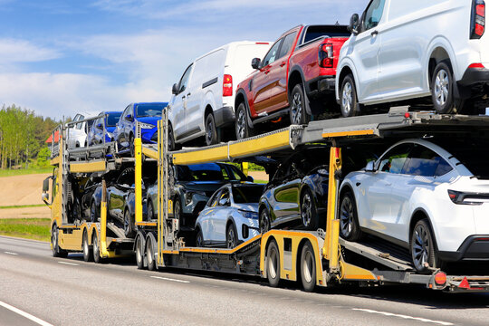Vehicle carrier truck at speed on road transporting new cars and vans stacked on trailer. 