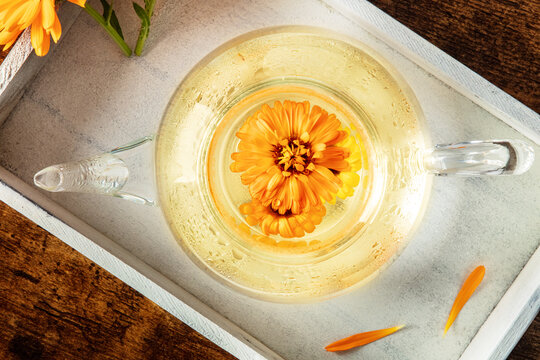 Fresh calendula herbal tea in a glass teapot, a flat lay