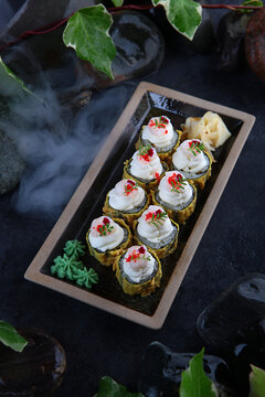 Rolls in tempura with mussels. Traditional Japanese cuisine. Raspberry tobik caviar. Ebi tempura. White ginger. Cocktail shrimp. Vertical photo on black background with smoke