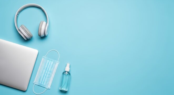 Remote Work Essentials with Laptop, Headphones, Face Mask and Hand Sanitizer on Blue Background