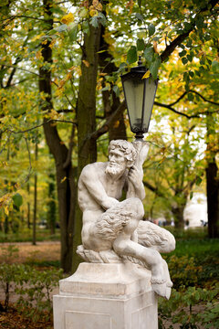 Ancient mythological faun sculpture built as a street light post amidst colorful autumn trees with yellow and green leaves.