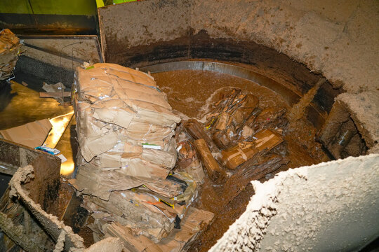 Cardboard boxes are broken down and pulped with water in a large, circular tank. This is part of the paper recycling process at a recycling plant or factory