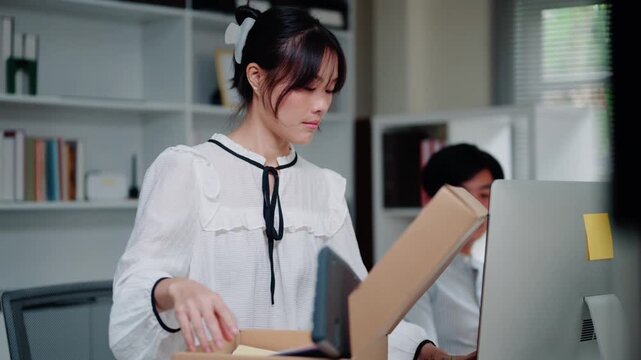 Asian Businesswoman Packing Personal Belongings in Cardboard Box After Being Sacked from Office Job