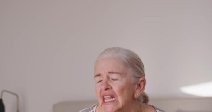 Senior woman wincing and gripping wooden cane, calling out in bed, shifting posture, gazing upward