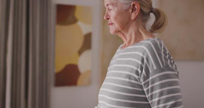 Senior female placing hand on cane for support, adjusting grip while standing taller in striped top