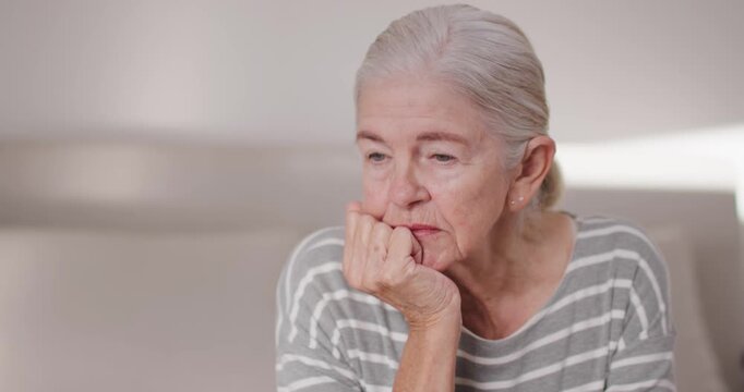 Senior woman on sofa, chin resting on fist, tracking offscreen motion, blinking, striped top, studs