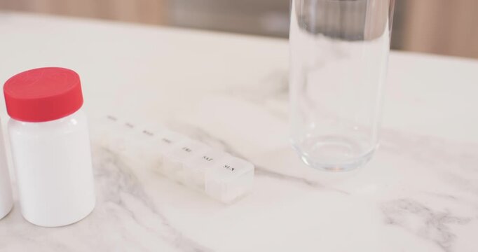 Camera is panning, two med bottles are sliding forward on marble counter beside pillbox for dosing