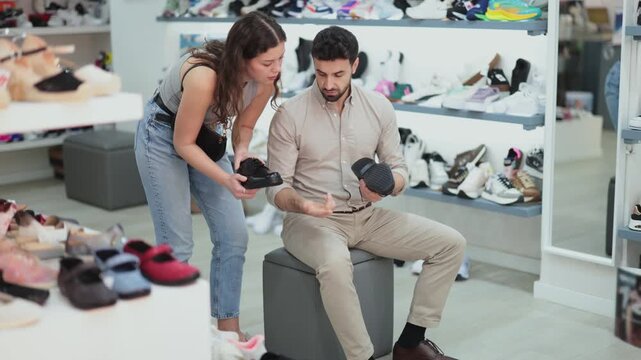 Man chooses classic shoes in a shoe store. Young woman helps him with this. High quality 4k footage