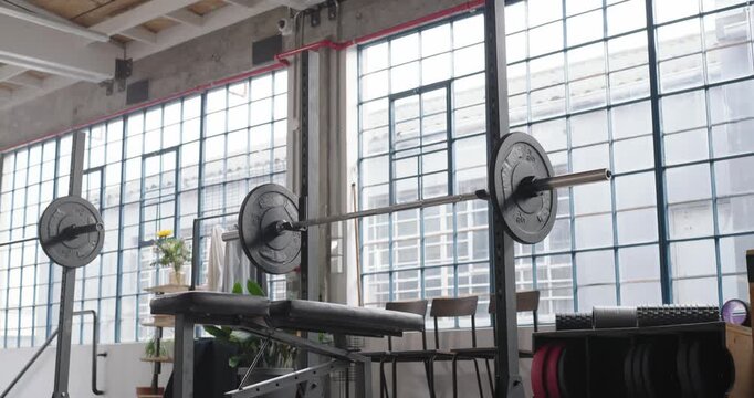 Camera is tilting down, revealing weight bench and loaded barbell on squat rack, showing loft gym