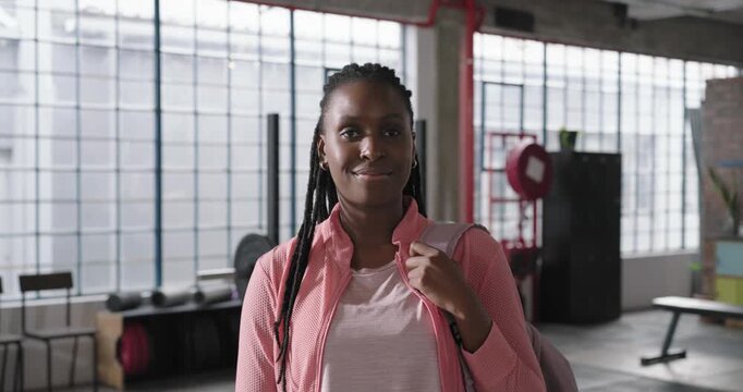 African American woman in pink jacket seeing camera turning holding backpack and smiling in studio