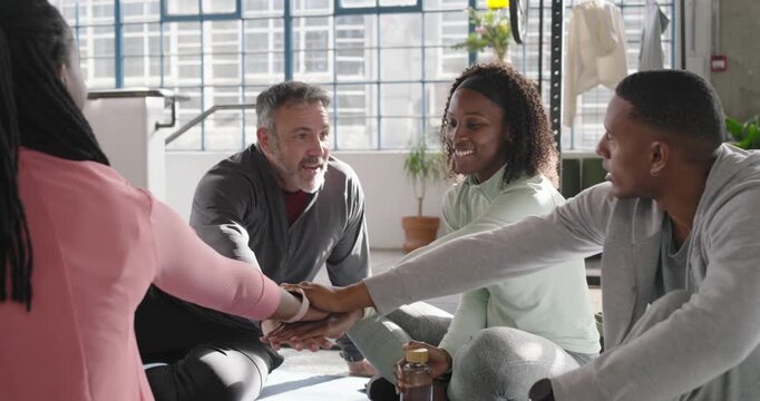 Diverse fitness group with middle-aged man speaking, reaching and stacking hands on yoga mats