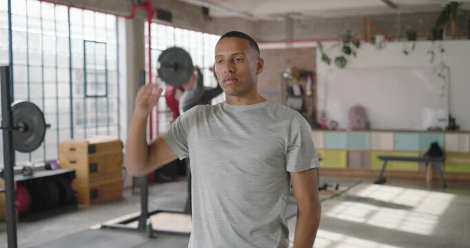 Man in gray tee stretching arms tilting neck warming up in gym studio by barbell rack