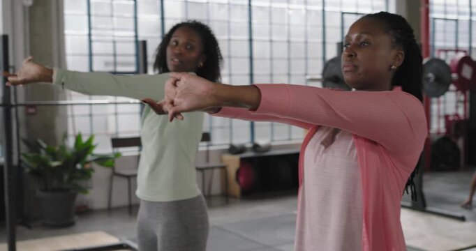 African American women in leggings starting arm stretch moving arms in sync near squat rack warming