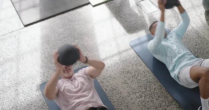 Diverse males holding lifting releasing catching medballs on blue mats in pink blue tops for core