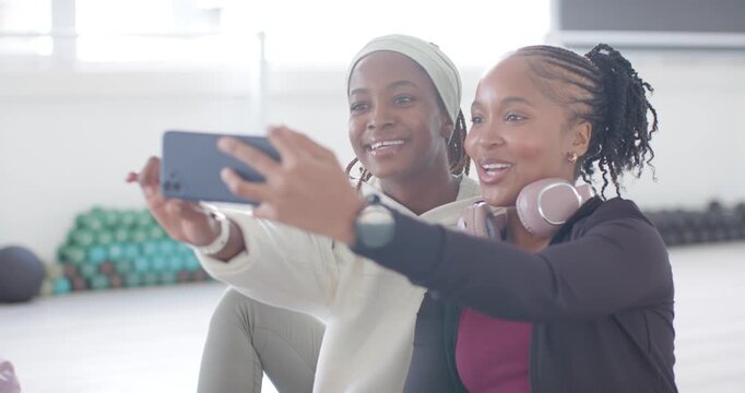 2 African women friends in workout clothes posing for selfie with phone in studio scrolling selfies