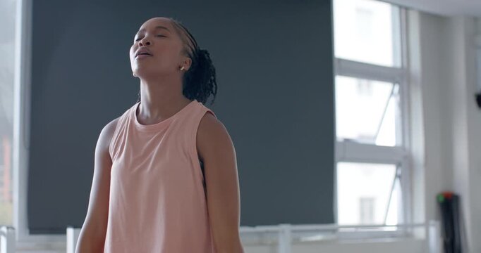 African woman ending shoulder raise in gym, placing hex dumbbell, checking smartwatch timing