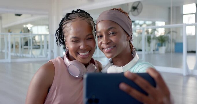 Two adult African women capturing selfie and reviewing blue smartphone at bright dance studio