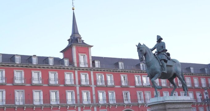 Equestrian statue in Madrid&rsquo;s Plaza Mayor with historic red facade, white windows and tower. Clear daytime view of one of the city&rsquo;s best known architectural landmarks.