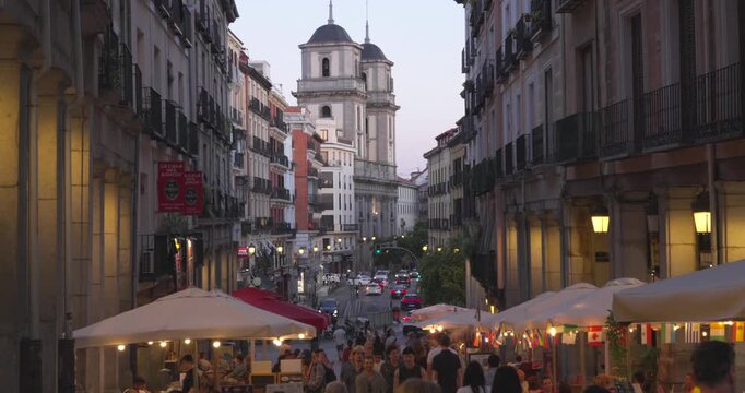 Madrid, Spain, July 4, 2026: Evening street view from Plaza Mayor toward San Isidro church. Restaurants, pedestrians and historic buildings create a lively urban atmosphere at dusk.