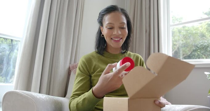 Adult African American woman placing box on lap opening box pulling jar checking label near window