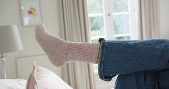 African American woman lying on bed lifting and flexing socked foot in cuffed jeans seeking rest