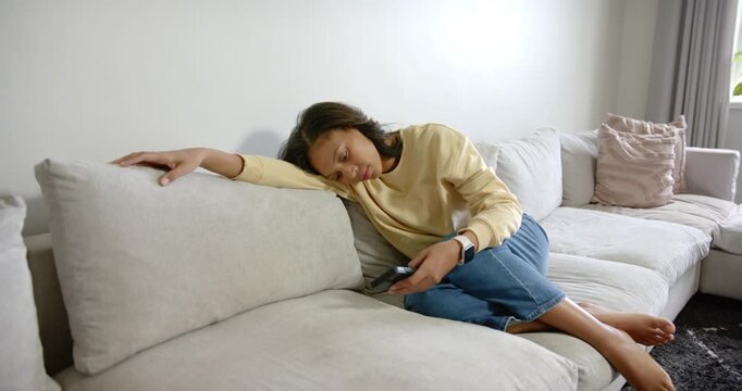 African American woman reclining on sofa at home after adjusting remote, watching TV and dozing