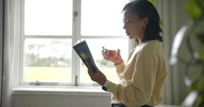 African American woman reading mag by window, light drawing focus, holding cup, wearing smartwatch