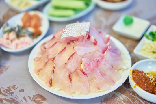 Premium raw croaker sashimi with traditional dipping sauces served for the summer boknal season. Captures authentic regional coastal gastronomy and is perfect for culinary travel or restaurant media.