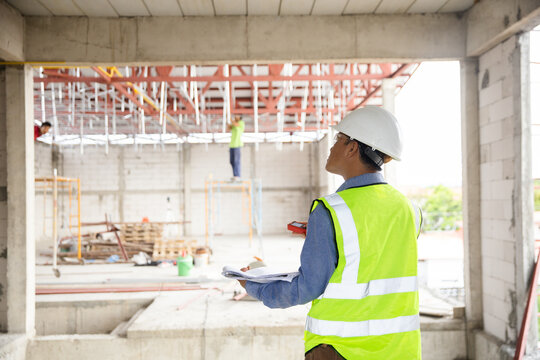 Construction engineer supervising a building site while workers in safety gear operate equipment and collaborate on various tasks