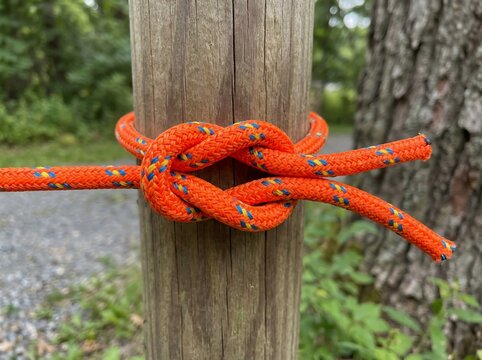 Orange rope tied in a reef knot around a wooden post
