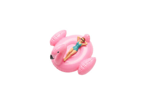 Miniature woman pink flamingo float sunbathing in swimsuit on white background. Tiny scale figure relaxing on inflatable pool toy, representing summer vacation travel concept and leisure lifestyle.