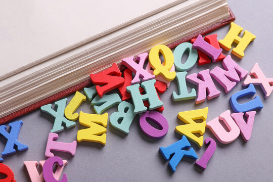 Book with many colored letters on gray background. Education, learning concept.