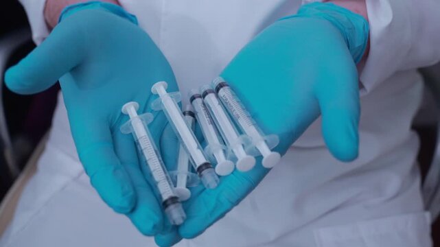 Healthcare professional wearing a lab coat and sterile gloves holding several unused injection syringes