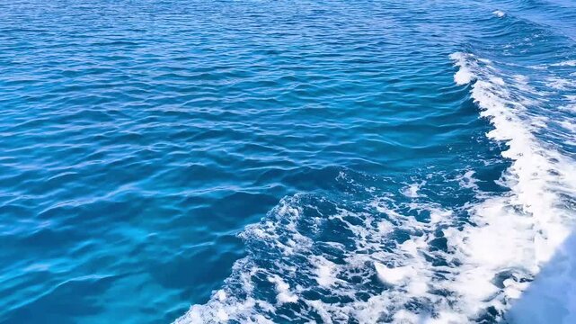 A side view of a boat leaving a white, foaming wake on the clear blue sea. A picturesque open-water seascape, perfect for travel, relaxation, and nautical themes.