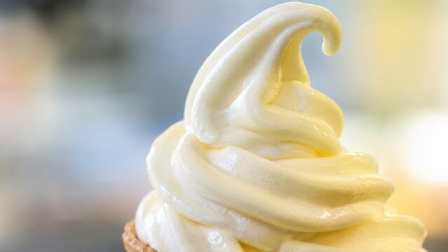 Close-up creamy vanilla soft-serve ice cream swirl in a cone, summer dessert with smooth texture and soft bokeh background