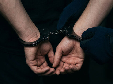 Close up of person hands in metal handcuffs isolated on a dark black background representing crime and arrest