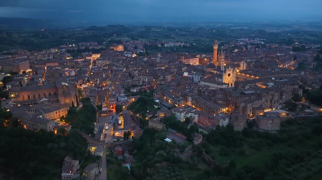 Siena, Italy. Aerial night 4K panoramic drone view of the city at dusk. Majestic view of the ancient city skyline with Basilica, Piazza del Campo, Duomo, iconic buildings. Europe from above.