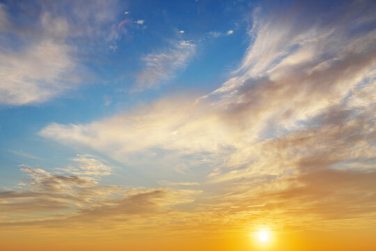 Golden sunset sky background with soft white and orange clouds under a blue sky.