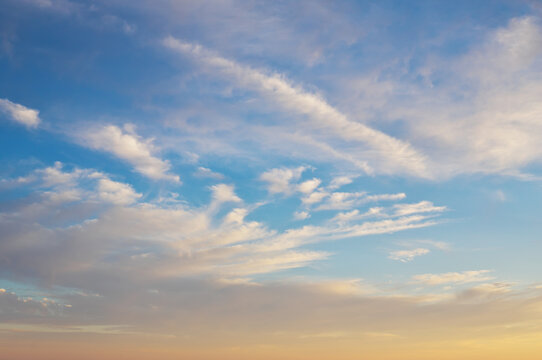 Blue sky background with soft white cirrus clouds and a warm pastel gradient at sunset.