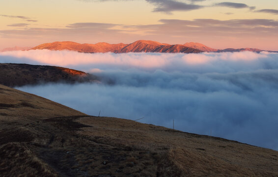 Fabulous sunset high in the mountains above the clouds. Aerial view of dramatic mountain landscape at dusk with fog and soft light.