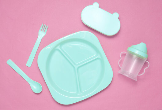 Set of plastic dishes for feeding baby and drinking bowls on pink background.