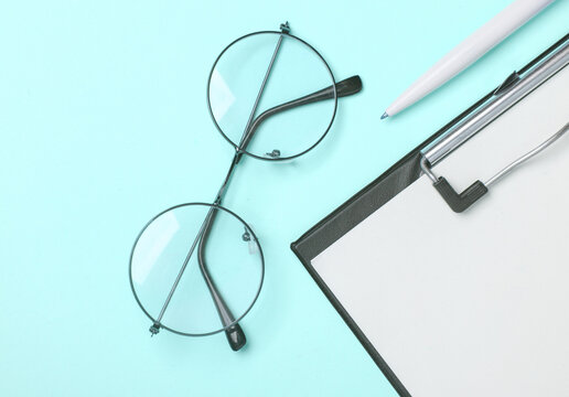Clipboard with eyeglasses on blue background. Business concept. Flat lay